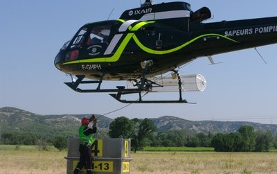 Un pompier accroche à l'hélicoptère le bac qui servira de réserve d'eau aux hommes en mission sur le massif - Photo Mathilde Boussion