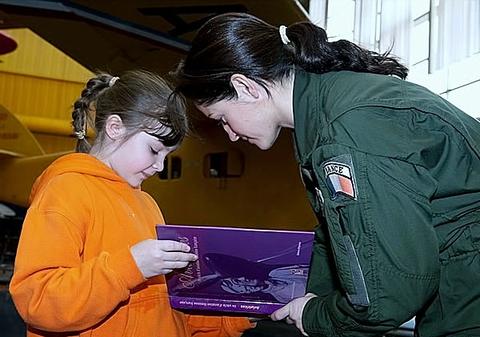 Une petite fille émerveillée s'approche d'une des pilotes (Le Capitaine Marie Macke, pilote de chasse de l'Armée de l'Air) et tend son livre sur les aviatrices pour avoir une dédicace - Photo Armée de l'Air
