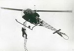 Le commandant Frédéric Curie est aux commandes du Bell 47 G2 avec Joseph de TADDEO accroché à l'échelle de corde de 8 m - Photo collection D. Roosens